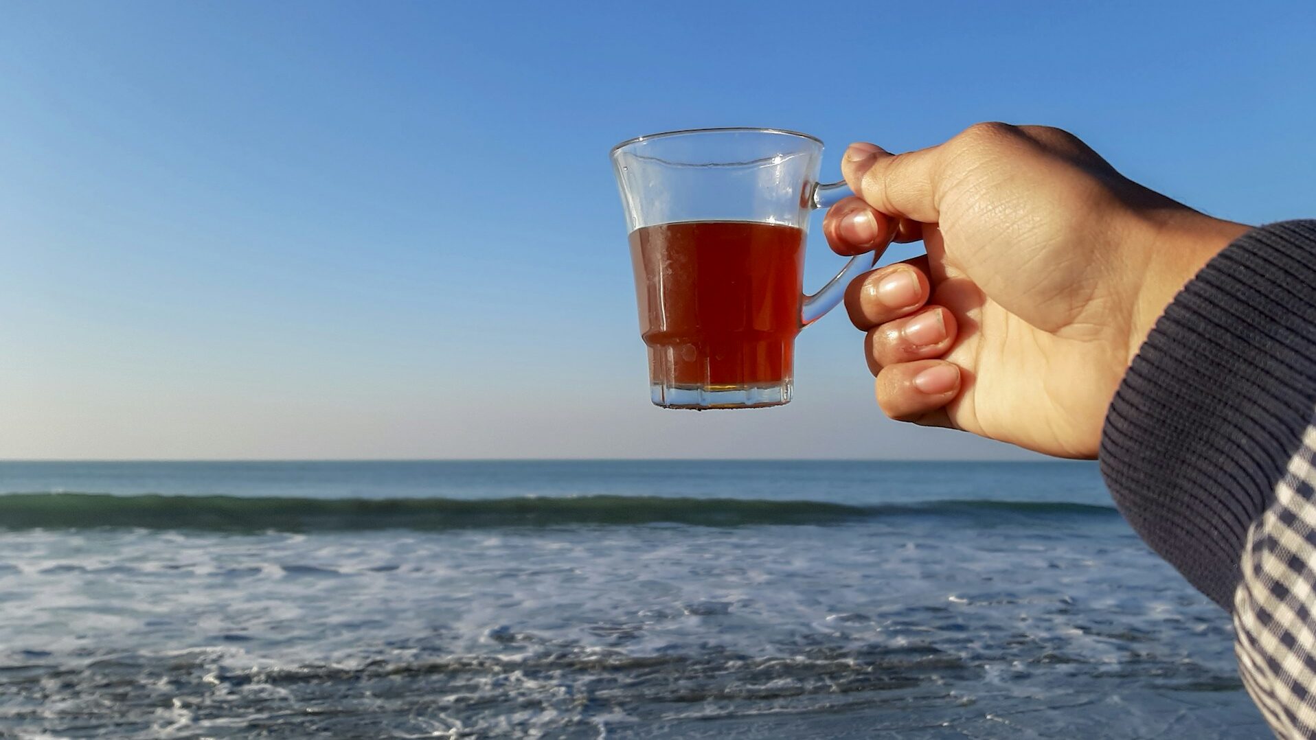 海辺でコーヒーを手に持つ